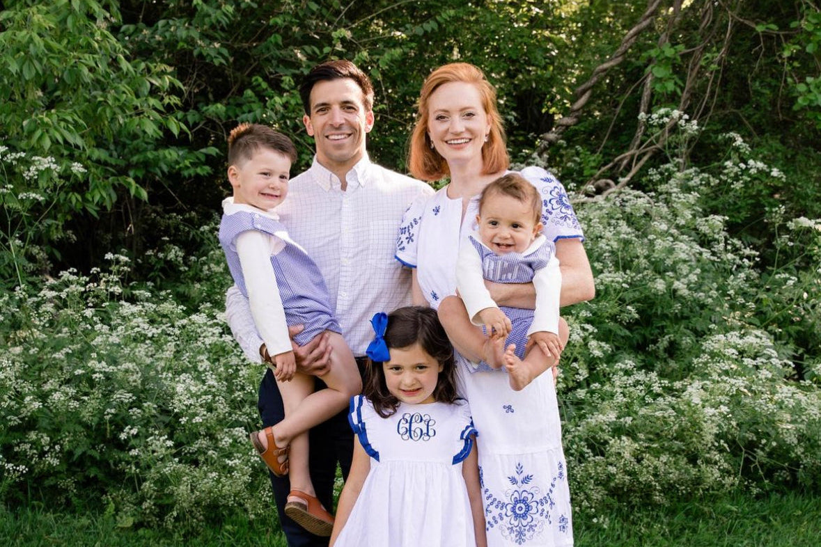 Family of four, two adults and two children, posing outdoors with greenery in the background.